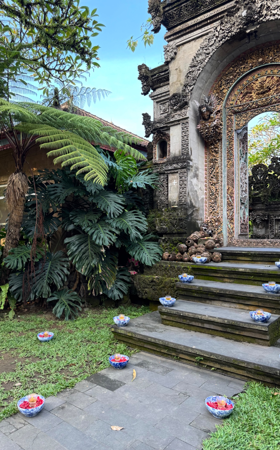 Carved Balinese temple gate framed by tropical ferns and offerings